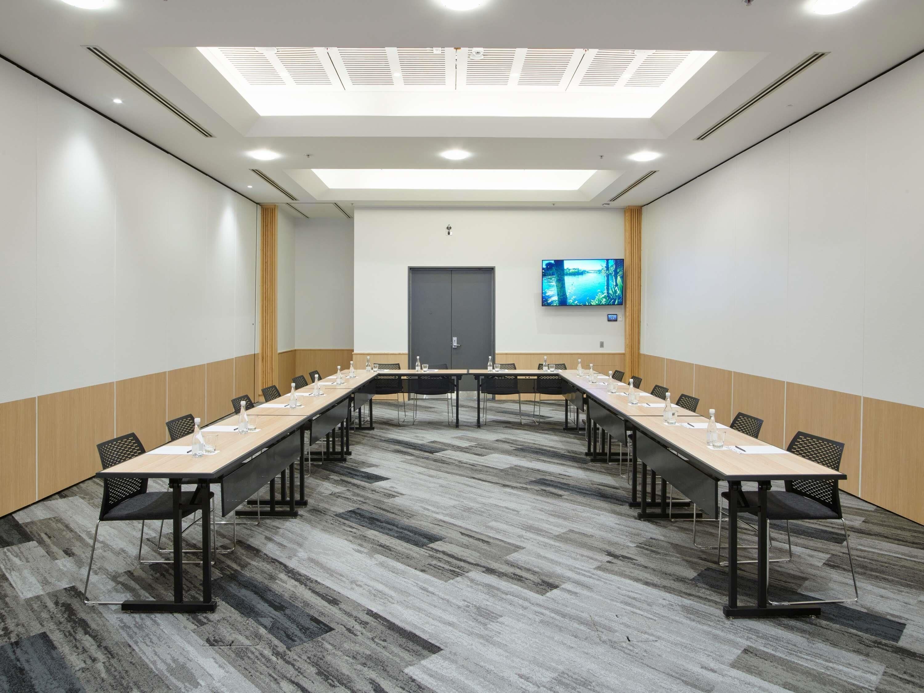 Un salón de conferencias con una mesa larga, sillas, un televisor de pantalla plana y una puerta.
