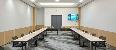 Un salón de conferencias con una mesa larga, sillas, un televisor de pantalla plana y una puerta.