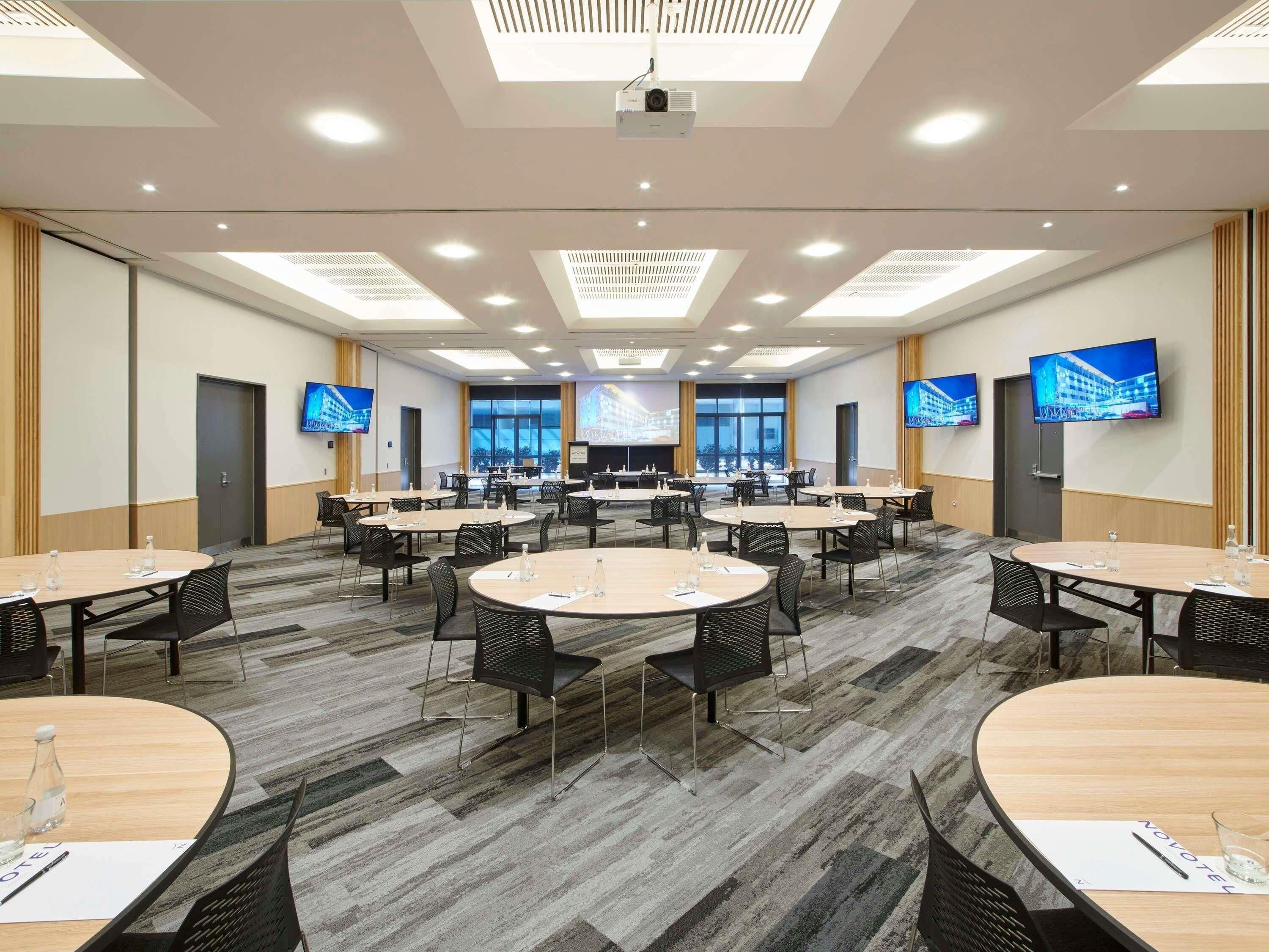 A conference room with multiple tables, chairs, and a large screen.