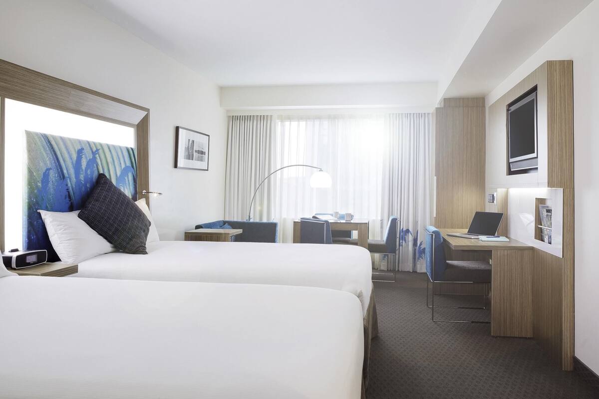 A hotel room with two beds, a desk, a chair, a TV, and a window with curtains.