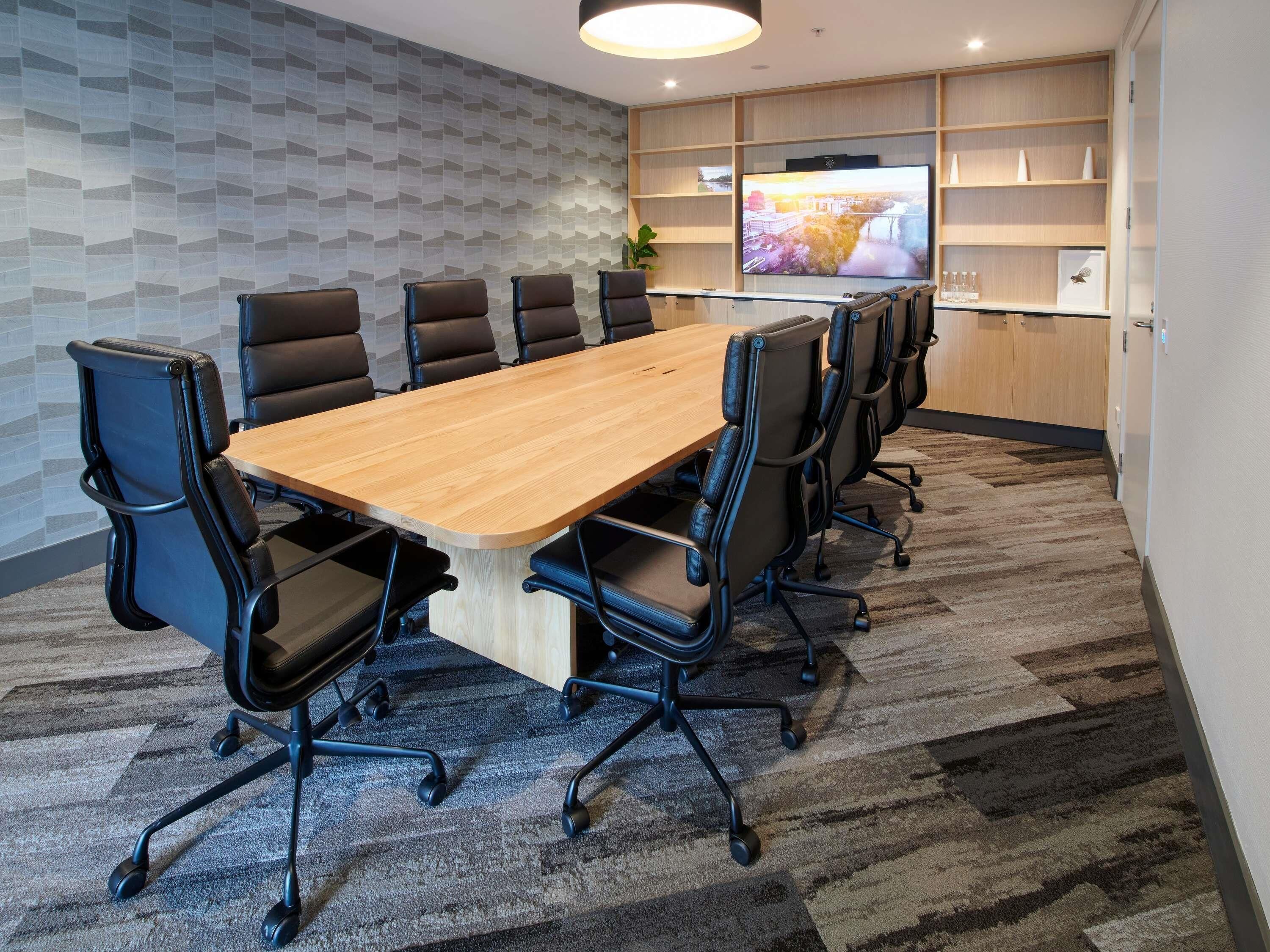 A conference room with a long table, black chairs, a TV on the wall, and a patterned wall.