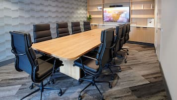 Un salón de conferencias con una larga mesa, sillas negras, un televisor en la pared y un diseño decorativo en la pared.
