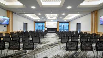 A conference room with rows of chairs, a large screen, and a projector.