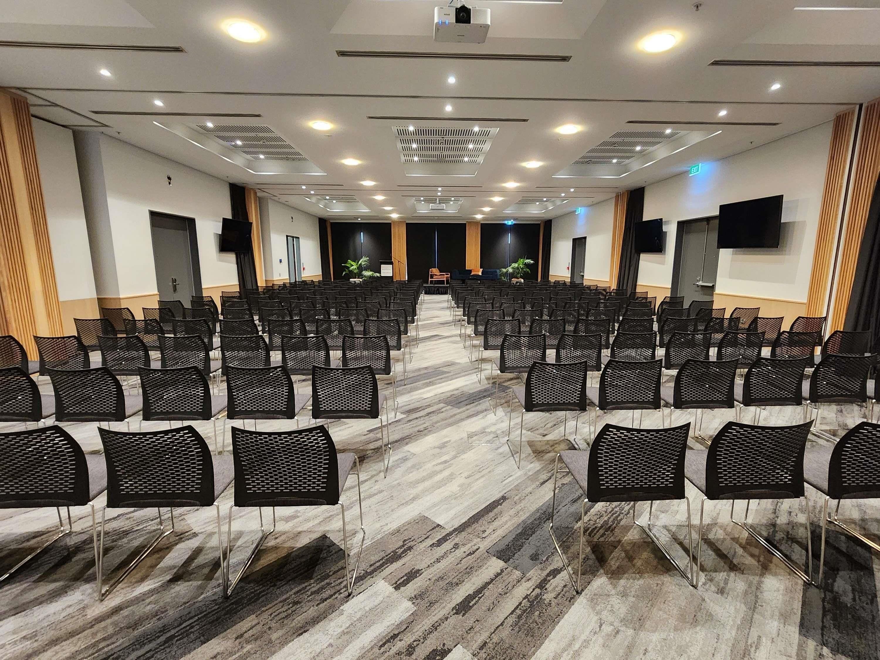 A conference room with rows of chairs, a stage, and a projector.