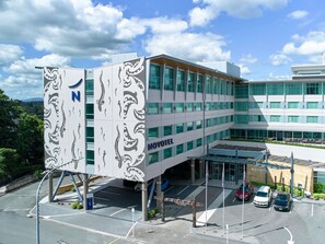 A modern hotel with a distinctive facade featuring a large 'N' and wave patterns, multiple floors, and a covered parking area.