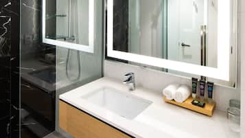 Uma casa de banho moderna com cabine de duche em vidro, um espelho grande e uma toucador com lavatório e gavetas de arrumação.