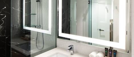 A modern bathroom with a glass-enclosed shower, a large mirror, and a vanity with a sink and storage drawers.