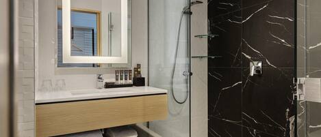 A modern bathroom with a glass-enclosed shower, a marble backsplash, and a vanity with a mirror and towel storage.