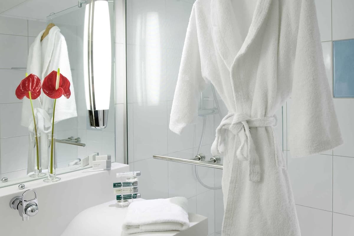 A modern bathroom with a white bathtub, a vanity with toiletries, a glass shower enclosure, and a white bathrobe hanging on a rack.