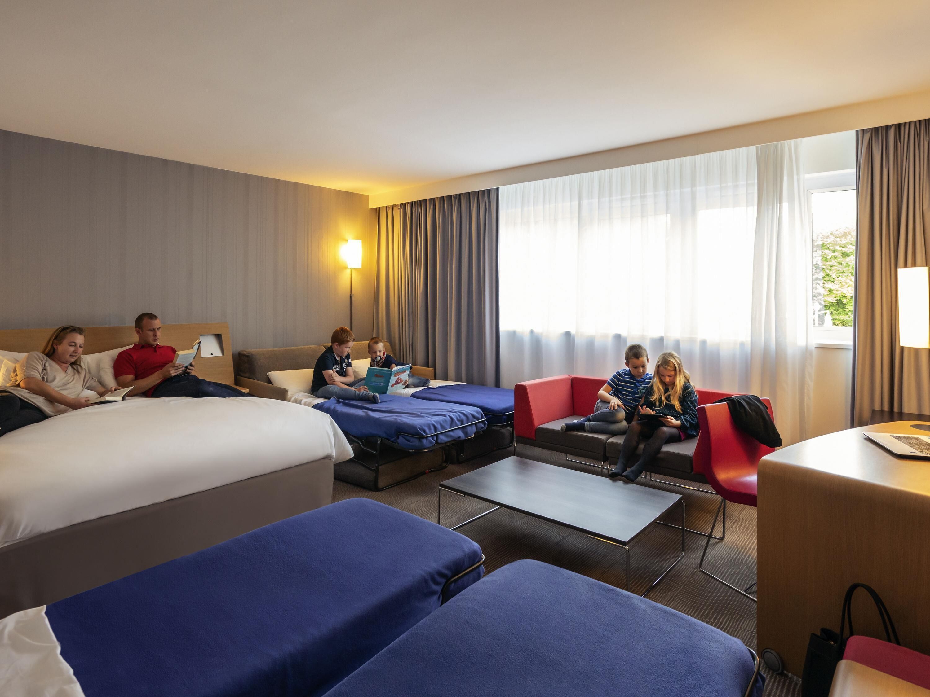 Habitación de hotel con cama, dos sofás, una mesita y ventana con cortinas.