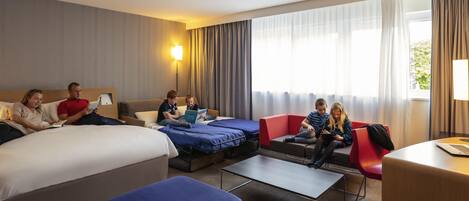 Habitación de hotel con cama, dos sofás, una mesita y ventana con cortinas.