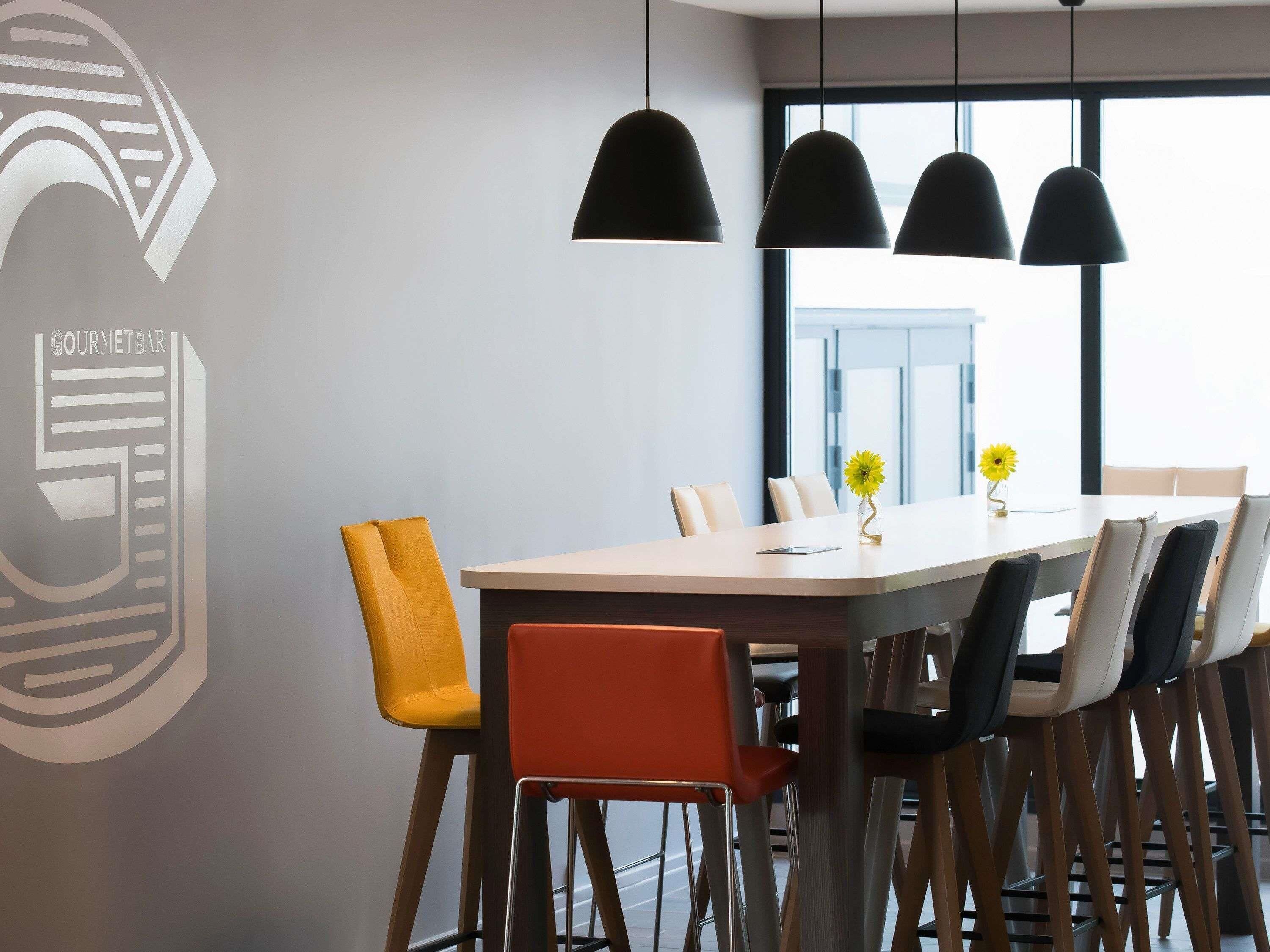 Een moderne eethoek met een lange tafel, meerdere stoelen, hanglampen en een raam met uitzicht.
