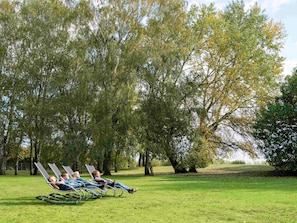 Three people relaxing on lawn chairs in a grassy park area with trees in the background. - Novotel Roissy Saint-Witz (Saint-Witz)