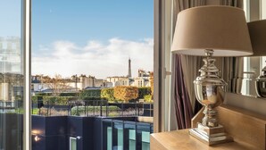 A modern hotel room with a large window offering a view of the Eiffel Tower and surrounding buildings.