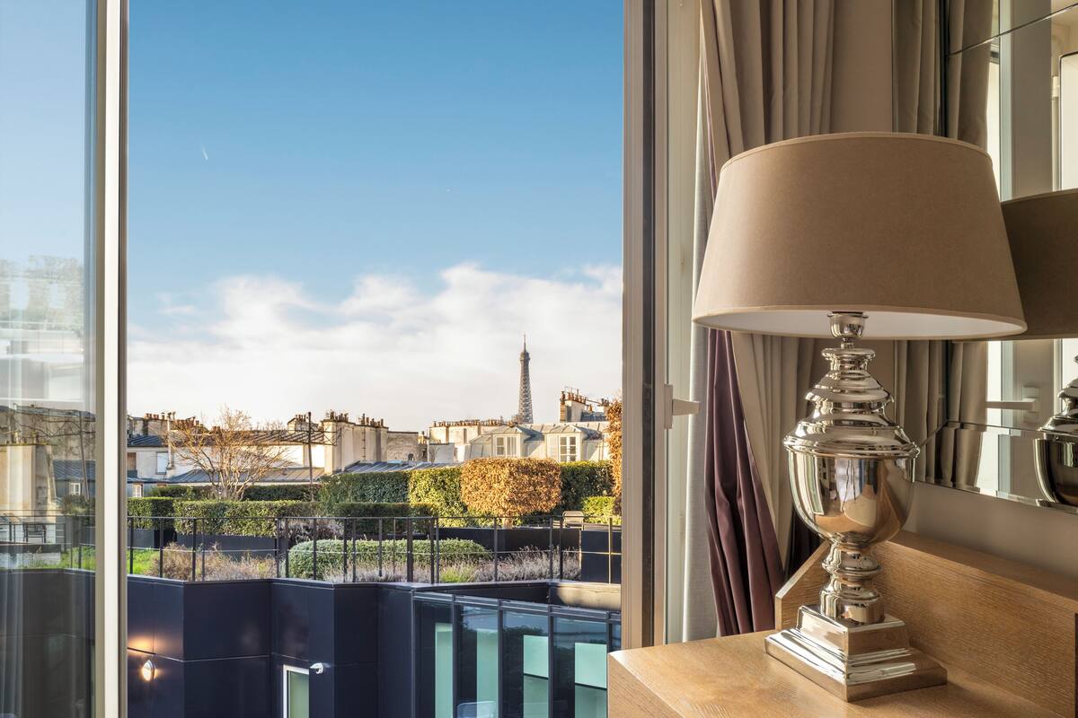 Habitación de hotel moderna con un gran ventanal que ofrece vistas de la Torre Eiffel y edificios circundantes.