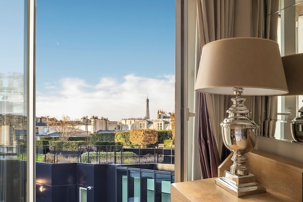 Habitación de hotel moderna con un gran ventanal que ofrece vistas de la Torre Eiffel y edificios circundantes.