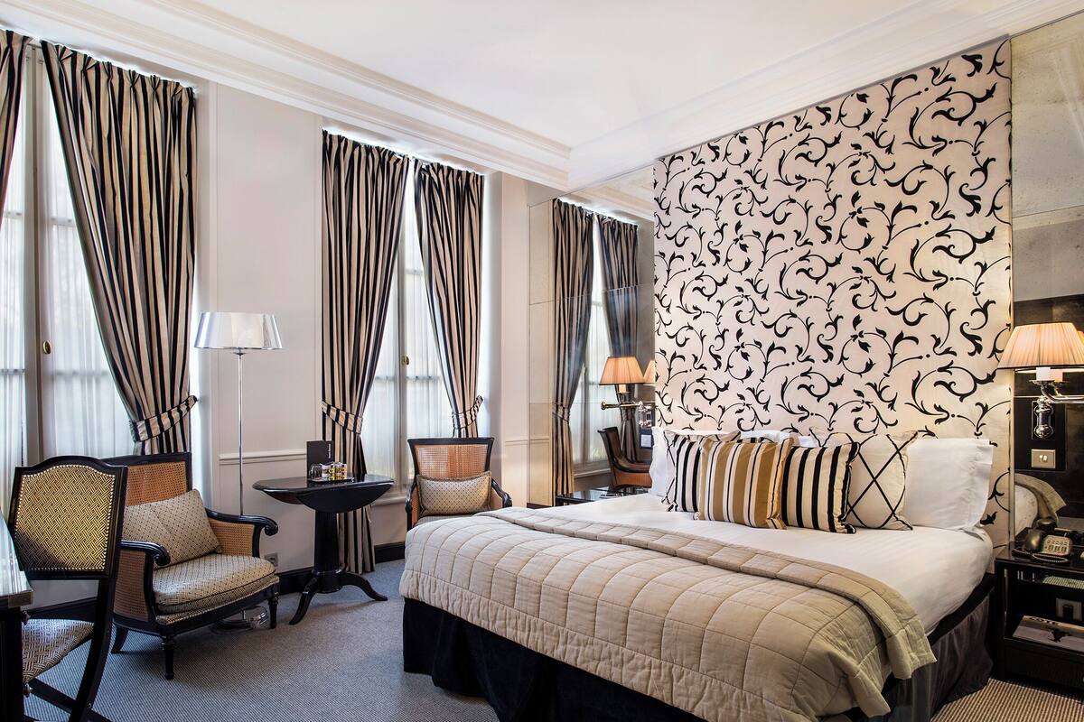 A hotel room with a large bed, two armchairs, a small table, and a lamp.