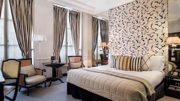 Una habitación de hotel con una cama grande, dos sillones, una mesita y una lámpara.