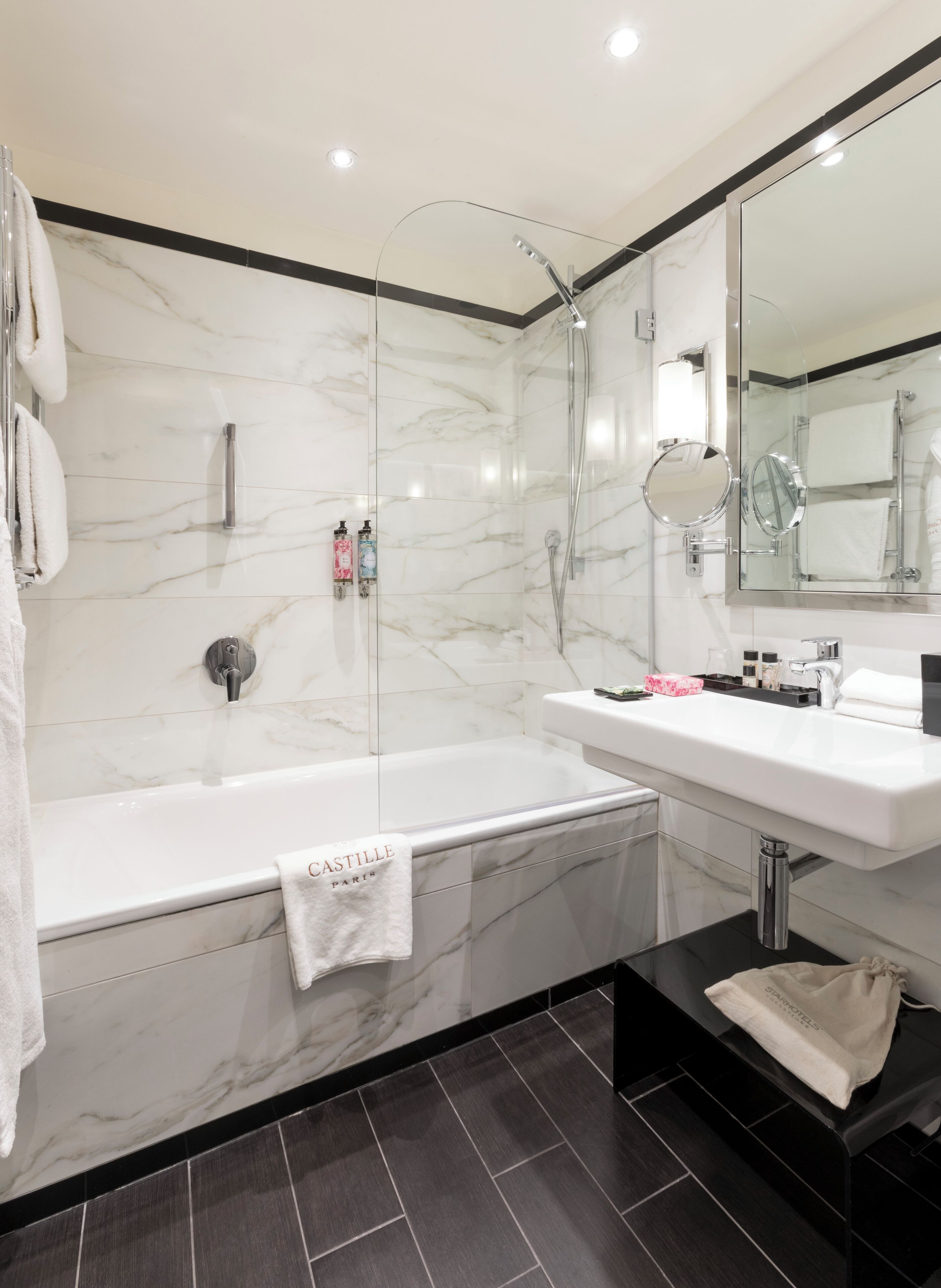 A modern bathroom with a glass-enclosed shower, a white bathtub, and a vanity with a mirror.