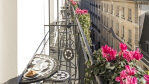 A balcony with a table and chairs, a potted plant with flowers, and a view of buildings. - Castille Paris - Starhotels Collezione (Paris)