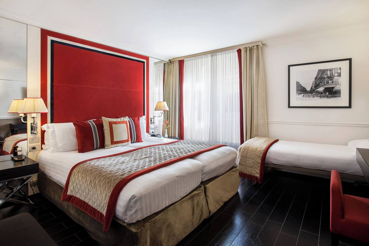 Habitación de hotel con una cama grande, una cama más pequeña, un escritorio y una silla.