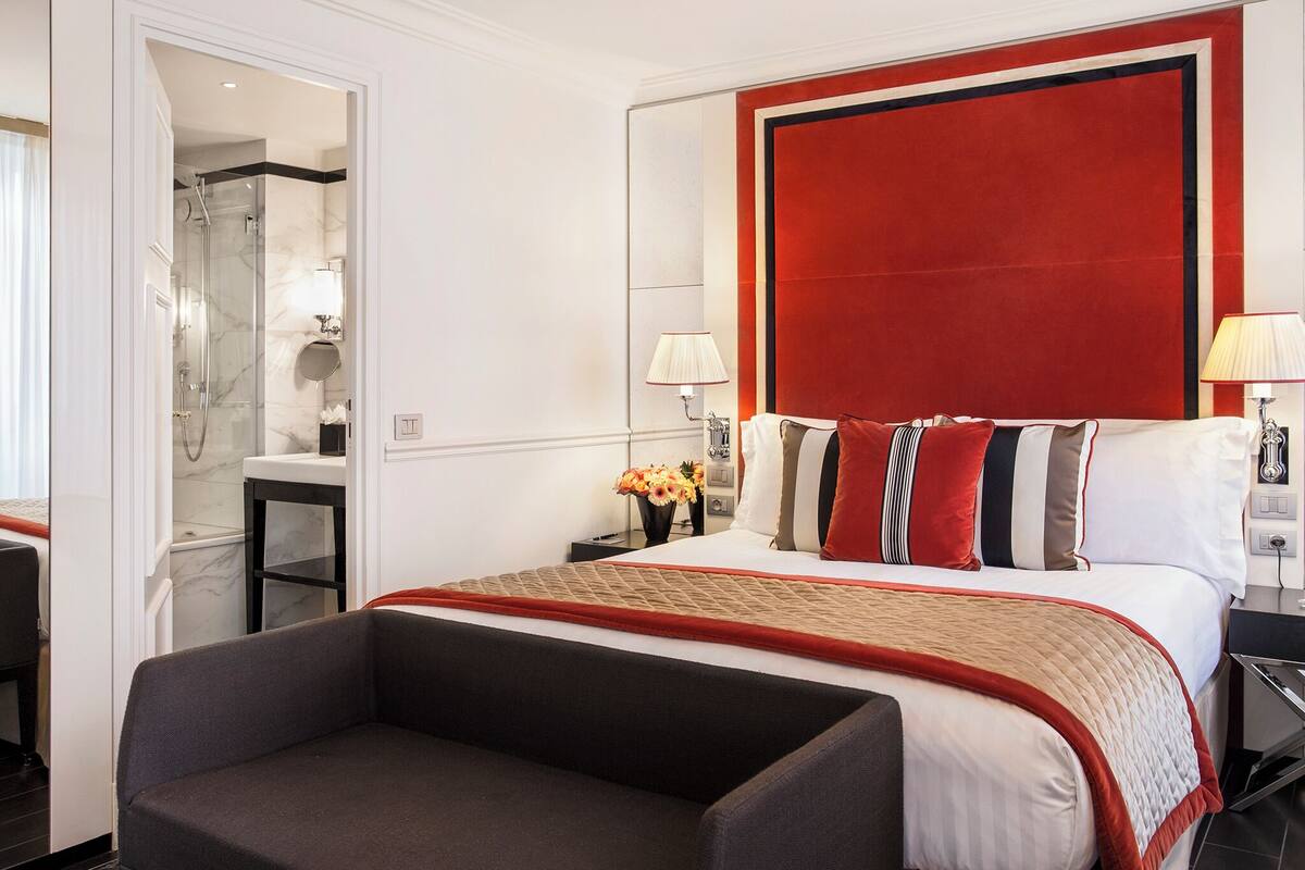 A hotel room with a large bed, a sitting area, a bathroom with a glass shower, and a red accent wall.