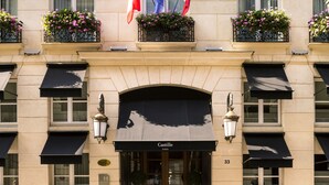 A hotel facade with multiple balconies, French and Italian flags, and a sign indicating the name and address.
