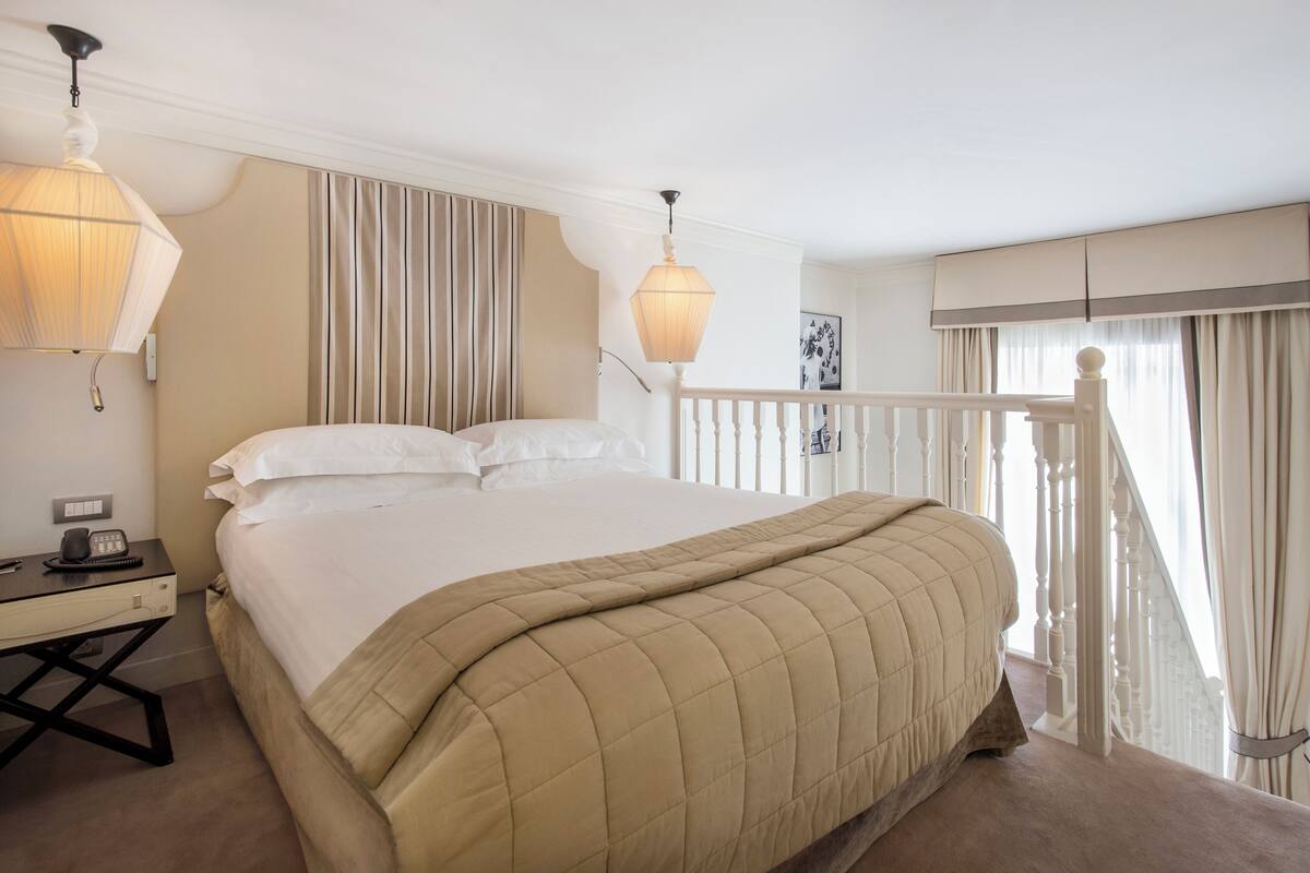 Habitación de hotel con una cama grande, un escritorio con teléfono y un balcón con barandilla.