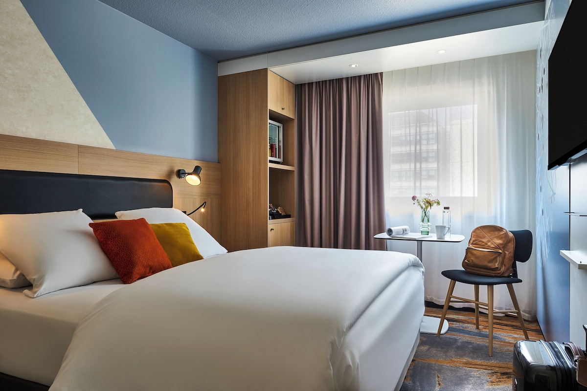 Een hotelkamer met een bed, een bureau, een stoel, een televisie en een raam met gordijnen.