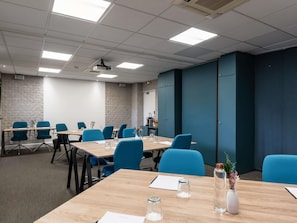 Un salón de conferencias con mesas, sillas y un proyector.
