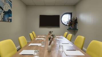 A conference room with a long table, yellow chairs, a large screen, and a window with a view.