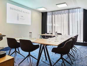 A conference room with a long table, chairs, a projector screen, and a large window with curtains.