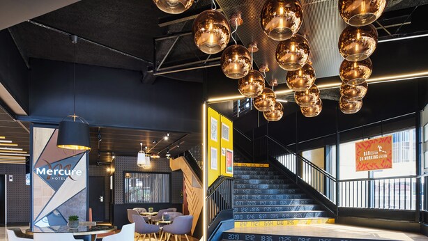 Een moderne hotellobby met een trap, een bar en zithoeken.