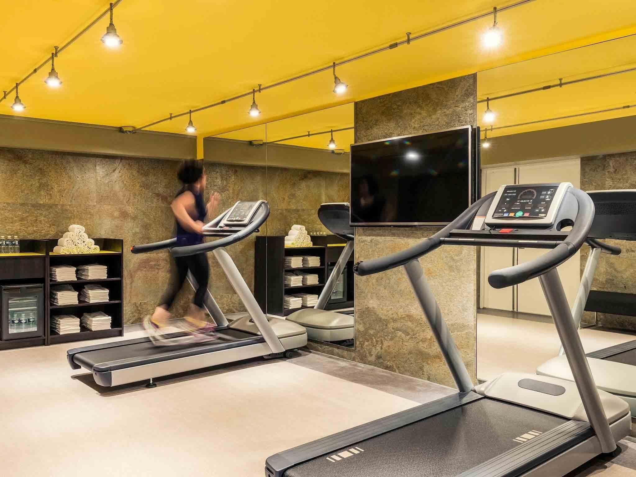Ein Fitnessraum mit Laufbändern, einem Fernseher und Regalen mit Handtüchern.