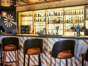 Een bar met verschillende flessen en glazen, een koffieapparaat en drie barkrukken.