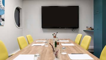 A conference room with a large flat-screen TV, wooden table, yellow chairs, and a teal cabinet.