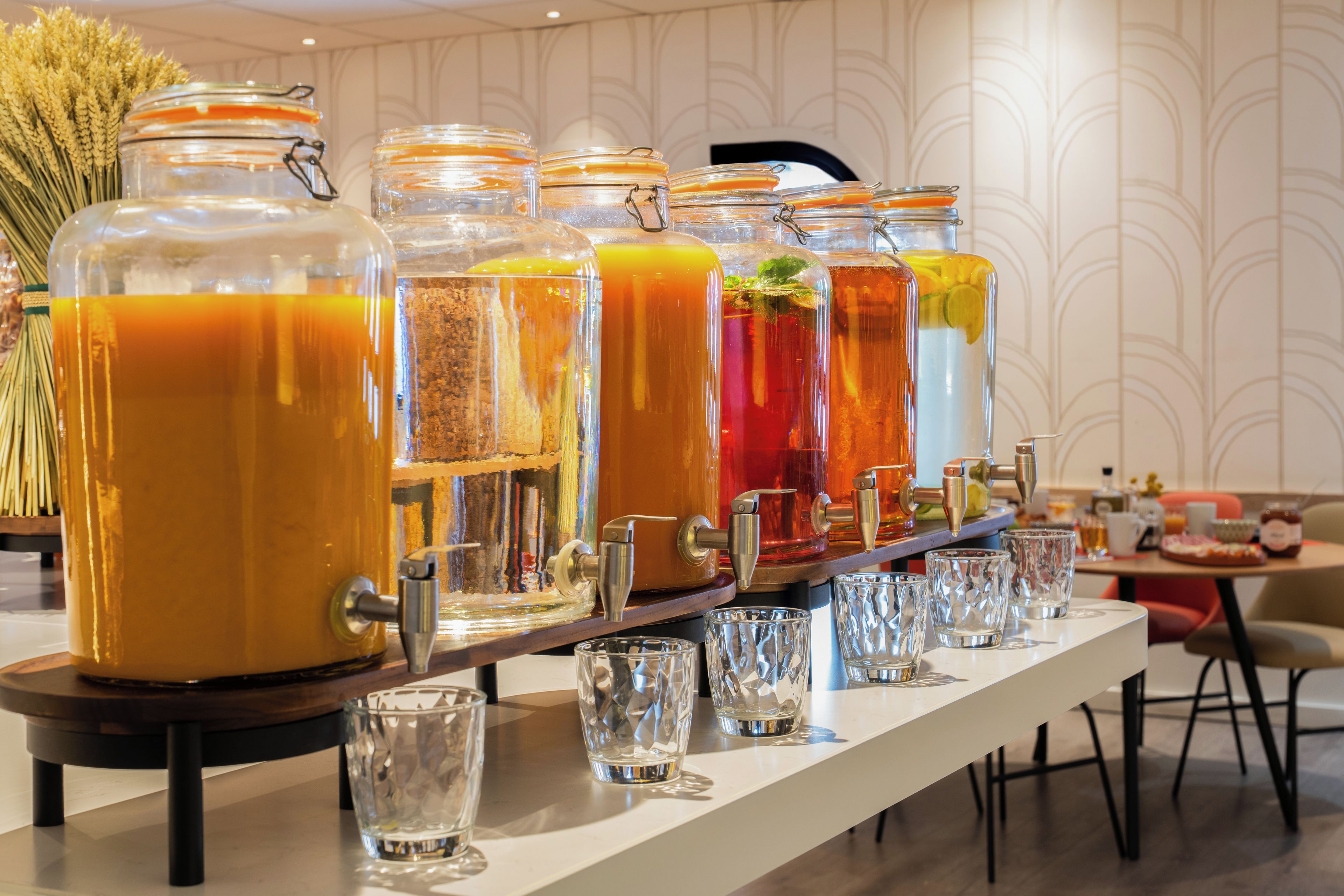 Un buffet de petit-déjeuner proposant diverses boissons servies dans de grands récipients et des verres, le tout disposé sur une longue table.
