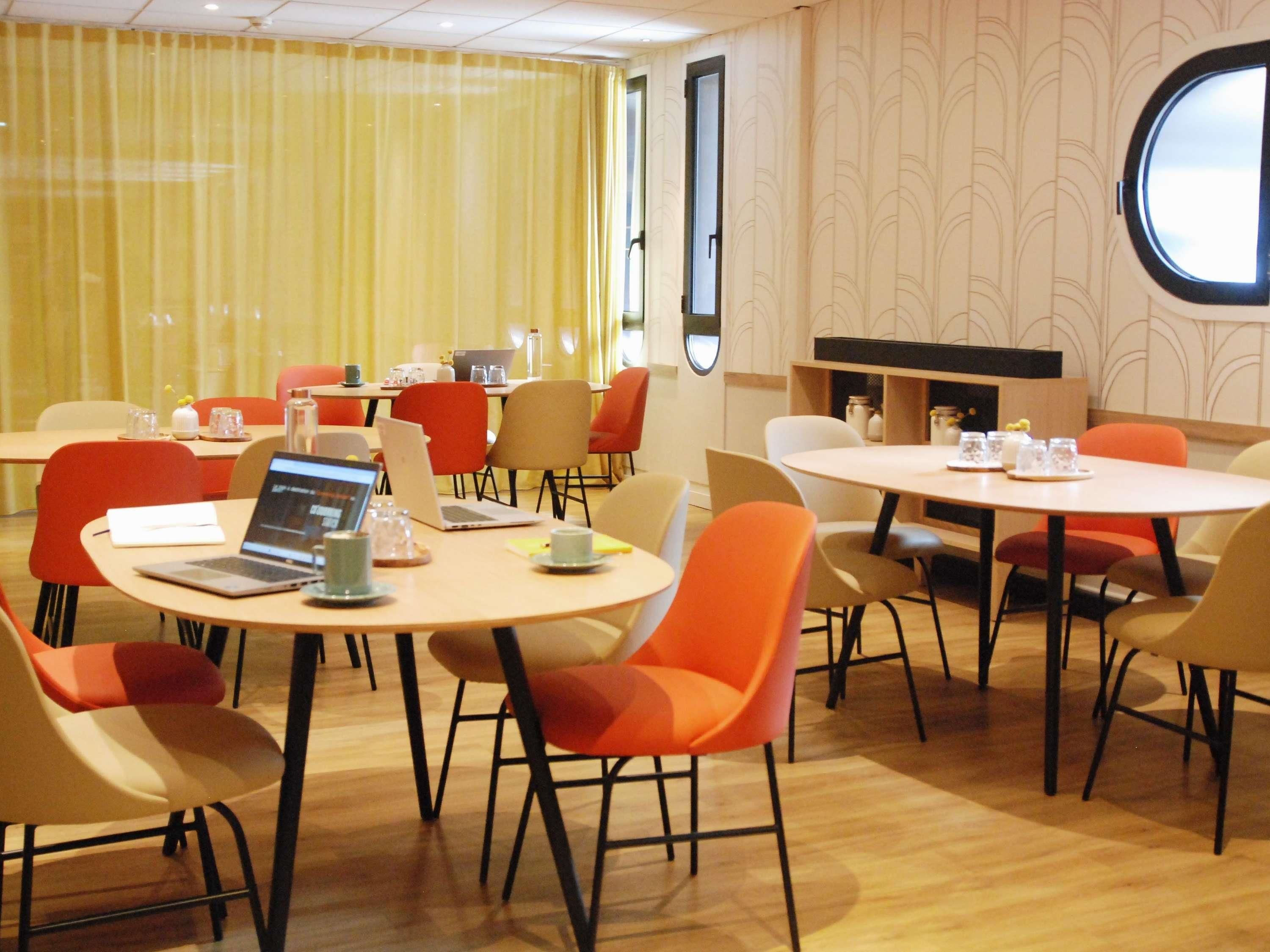 A conference room with round tables, chairs, laptops, and a large window.