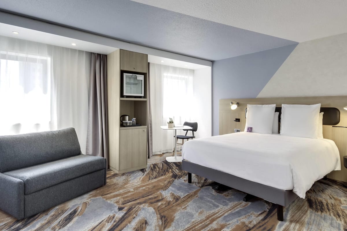 A hotel room with a bed, a sofa, a desk, and a TV.