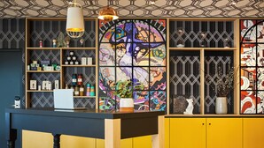 Een modern interieur met een eilandtafel in het midden, houten planken met verschillende spullen, en een kleurrijk glas-in-loodraam.