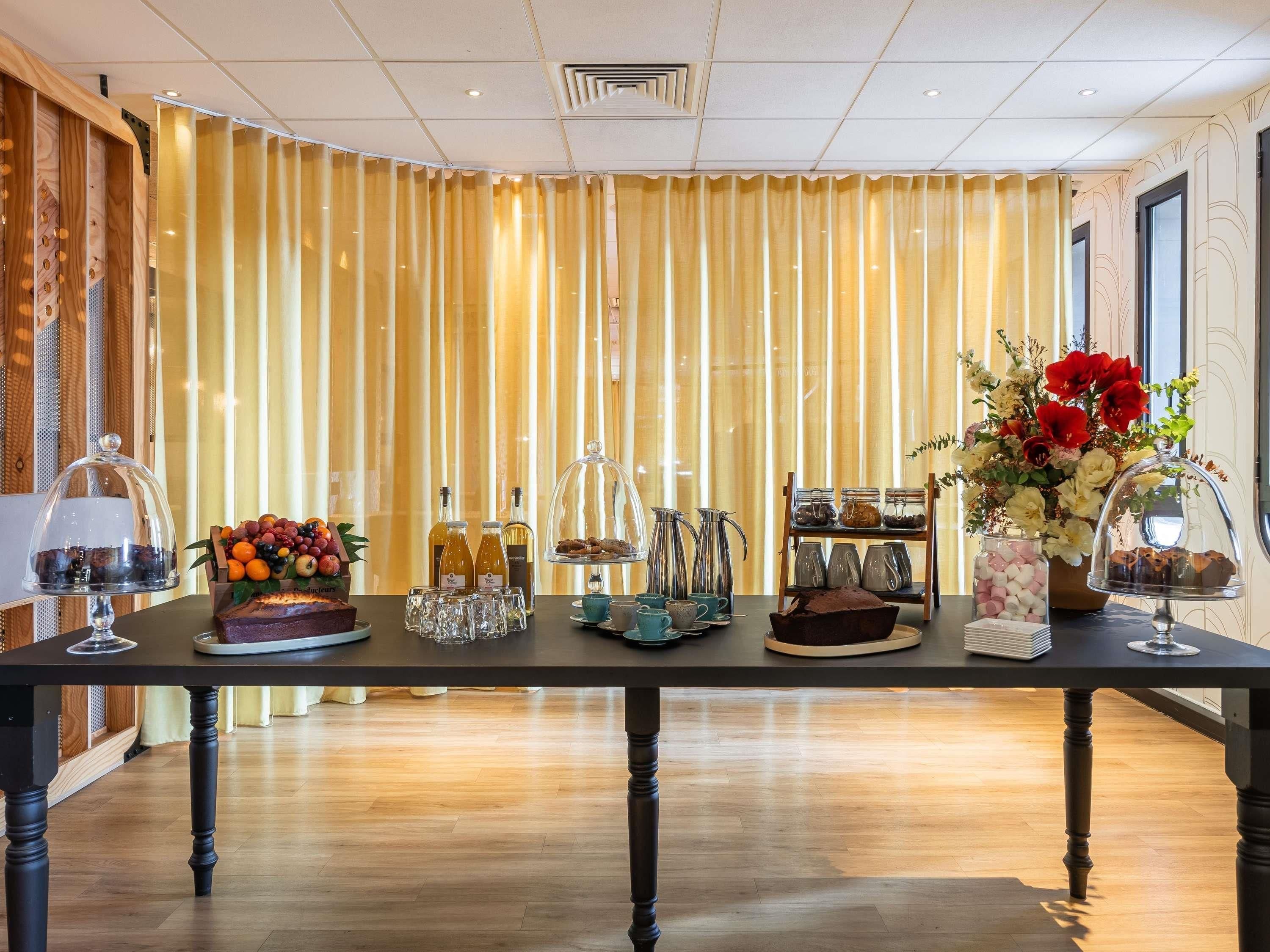 Habitación de hotel con una larga mesa dispuesta con diversos elementos, incluyendo una presentación de frutas, botellas y un arreglo floral.