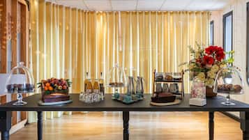 Habitación de hotel con una larga mesa dispuesta con diversos elementos, incluyendo una presentación de frutas, botellas y un arreglo floral.