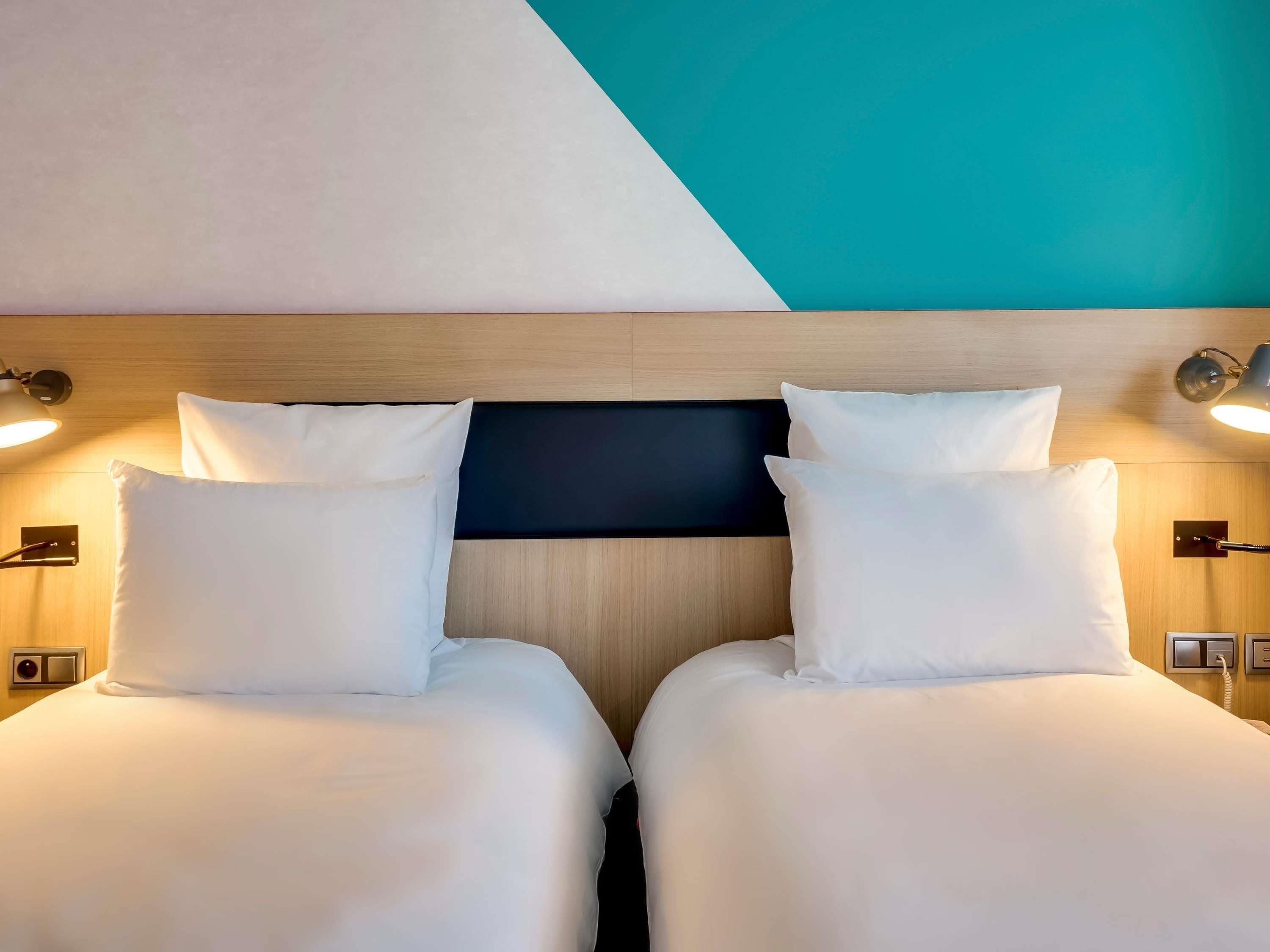 Une chambre d’hôtel avec deux lits, une tête de lit en bois, des lampes de chevet et un téléviseur fixé au mur.