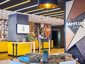 A hotel lobby with a reception desk, a large chandelier, and a wall with a clock illustration.