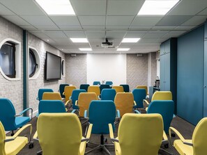 Un salón de conferencias con techo blanco, paredes de ladrillo gris y una puerta azul.