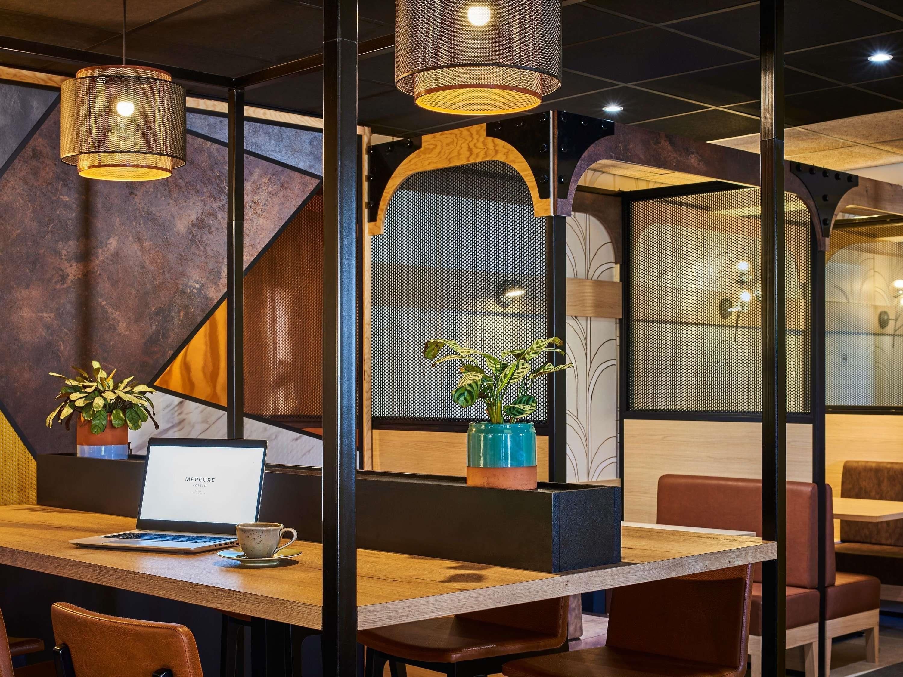 A modern interior with wooden tables, metal partitions, and hanging lamps.