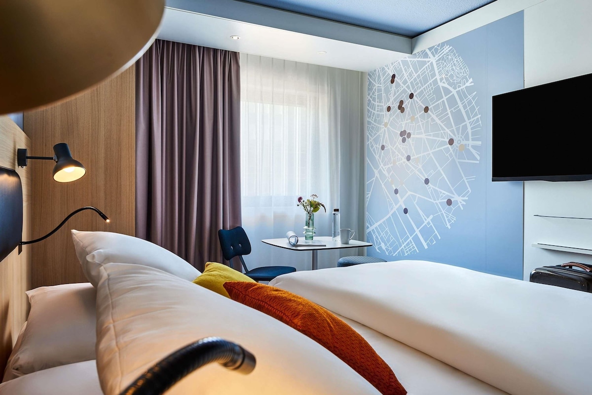 Et hotelværelse med en seng, et skrivebord med stol, et fjernsyn og en væg med et verdenskort-design.