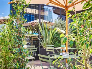 An outdoor seating area with green chairs and umbrellas, a glass storefront with 'CORNER TATION' signage, and various plants. - Mercure Paris Gare De Lyon TGV (Paris)