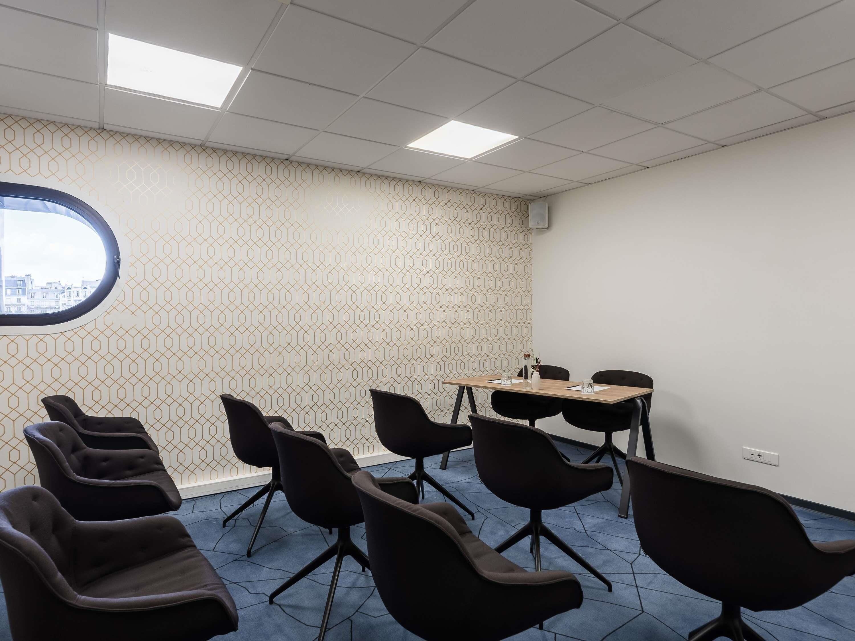 Un salón de conferencias con un papel tapiz decorativo, un ventanal grande y varias sillas y mesas.
