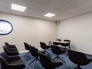 Une salle de conférence avec un mur décoré de motifs, une grande fenêtre, ainsi que plusieurs chaises et tables.